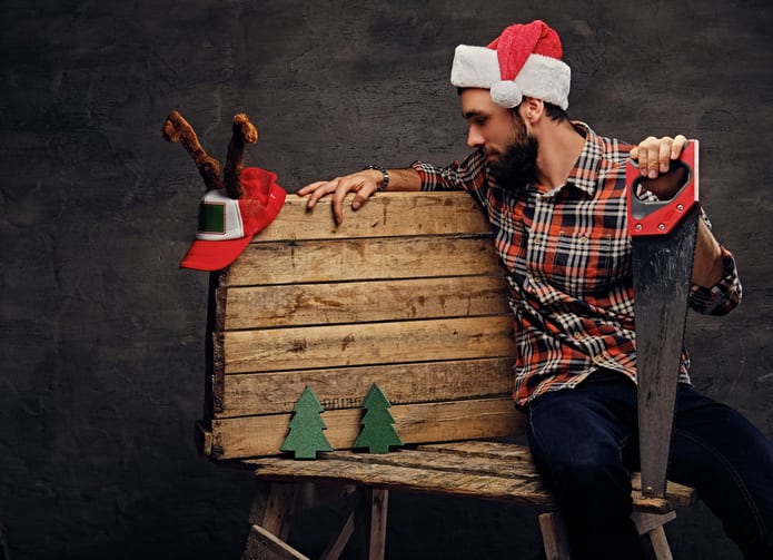 Oswald Wholesale Lumber Christmas and New Year scene. Bearded male in Santa's hat sits on wooden palette with fir trees and holds handsaw.